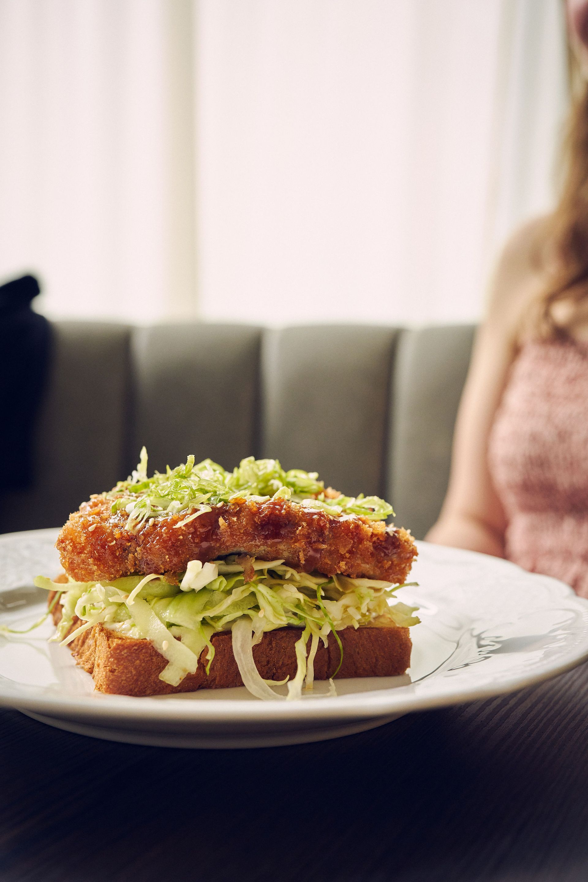 Sprøstekt sandwich på en tallerken med strimlet kål, i en restaurantsetting.
