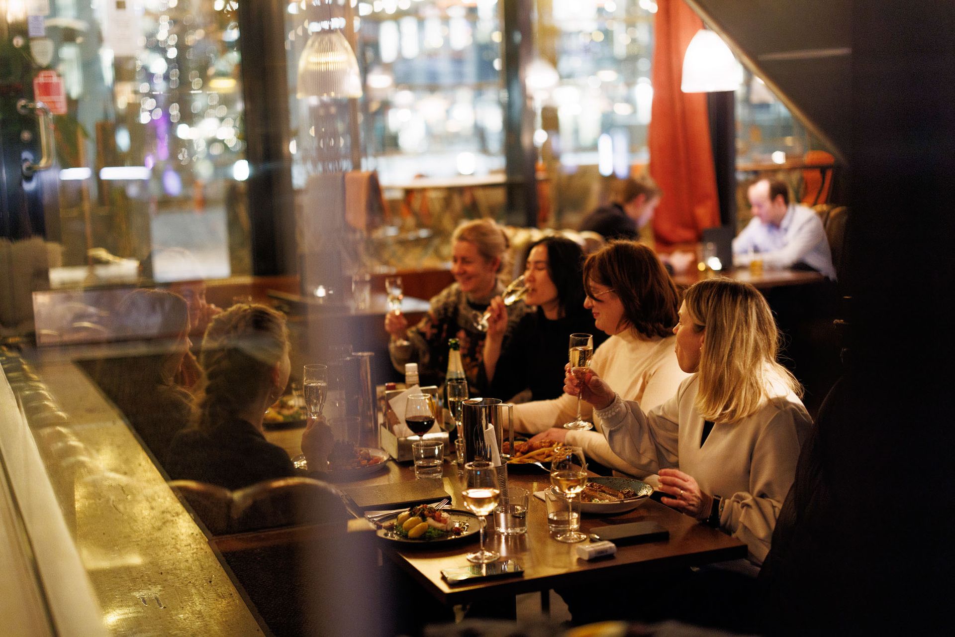 En smilende mann spiser salat med en drink ved et bord. Sollys strømmer inn fra et vindu.