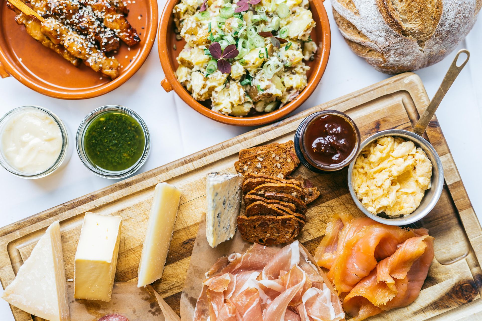 Charcuterie-brett med ost, kjøtt, kjeks og dipper, omgitt av andre retter.
