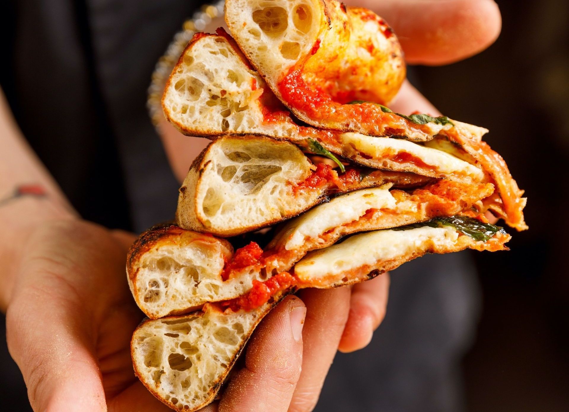 En person holder en sandwich med tomatsaus og ost i hendene.