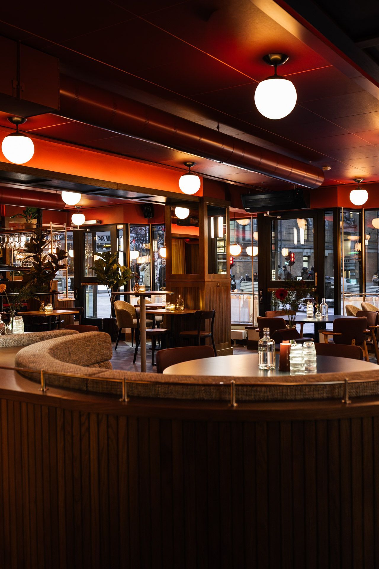 Interiør i en svakt opplyst restaurant med trepanel, runde bord og globuslys.