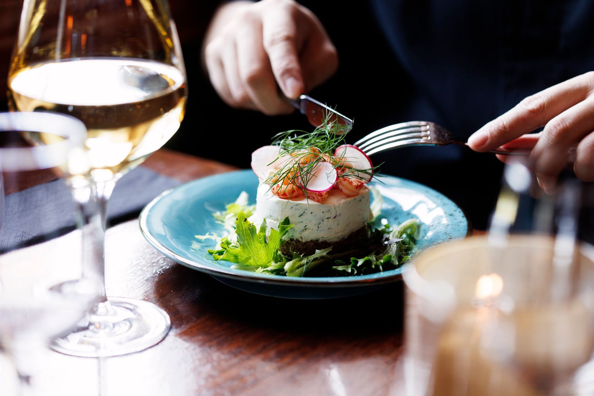 En person sitter ved et bord med en tallerken mat og et glass vin.