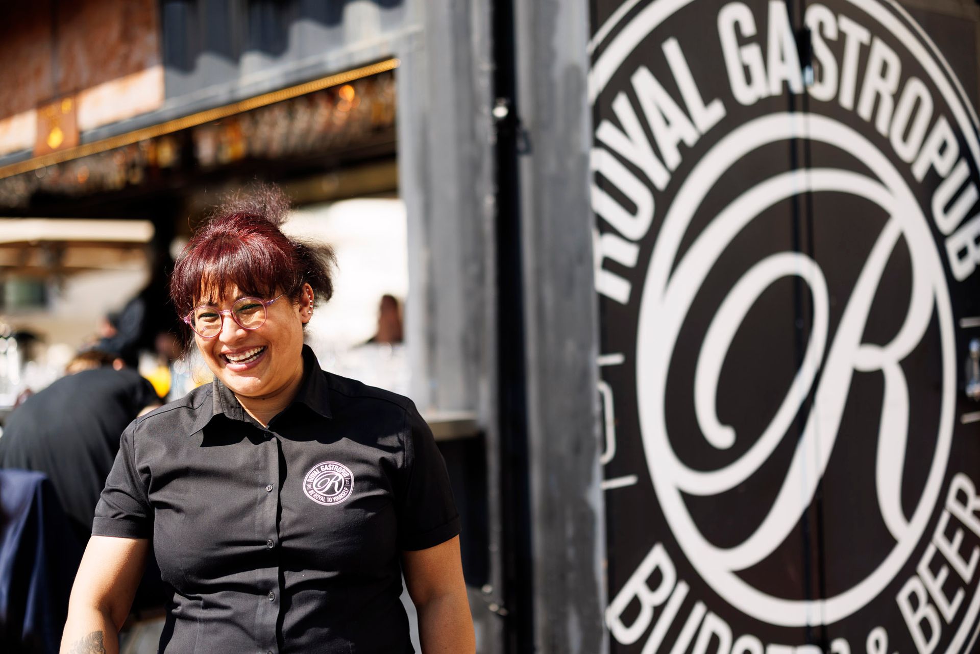 Smilende kvinne i svart skjorte foran skiltet «Royal Gastropub».