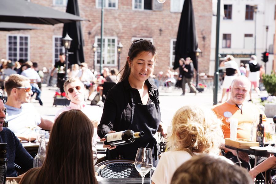 En kvinne serverer vin til en gruppe mennesker på en restaurant.