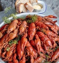 En skål med kreps sitter på et bord ved siden av en bolle med brød.