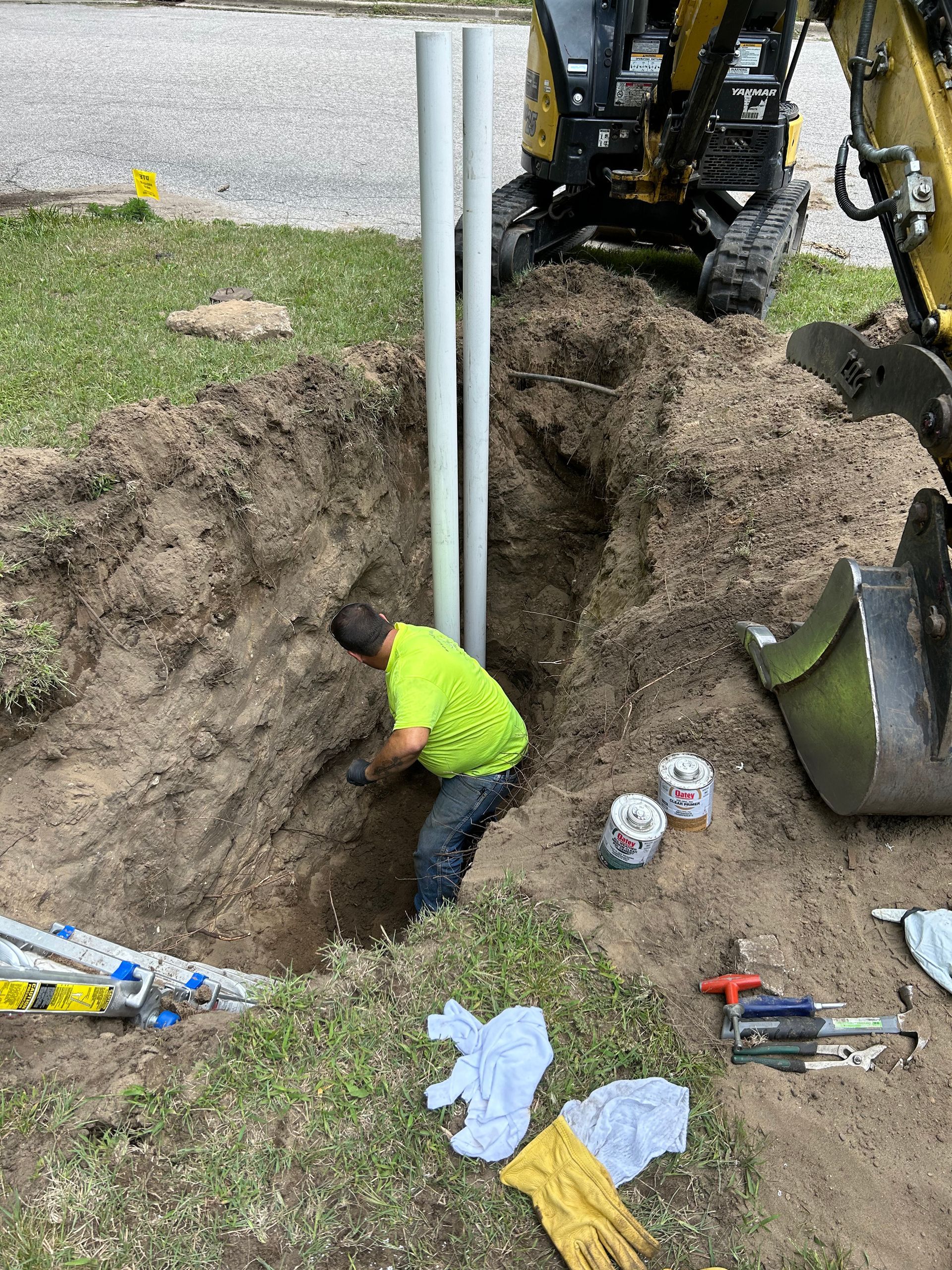 A man is digging a hole in the ground next to a yellow excavator.