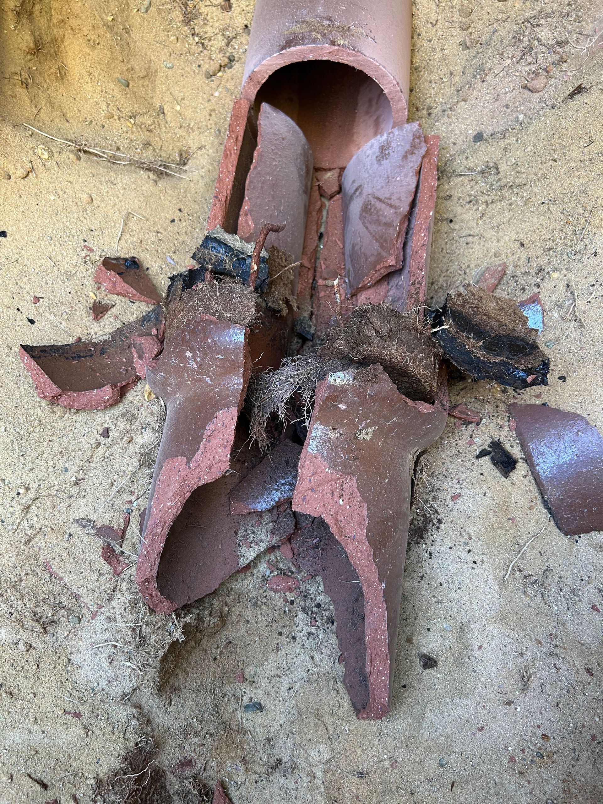 A broken pipe is laying on the ground in the sand.