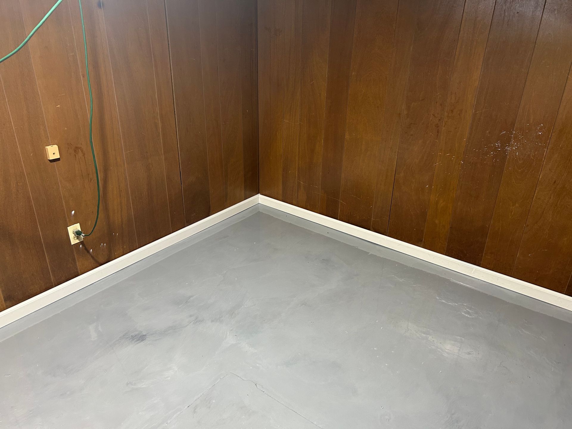 A corner of a room with a concrete floor and wooden walls.