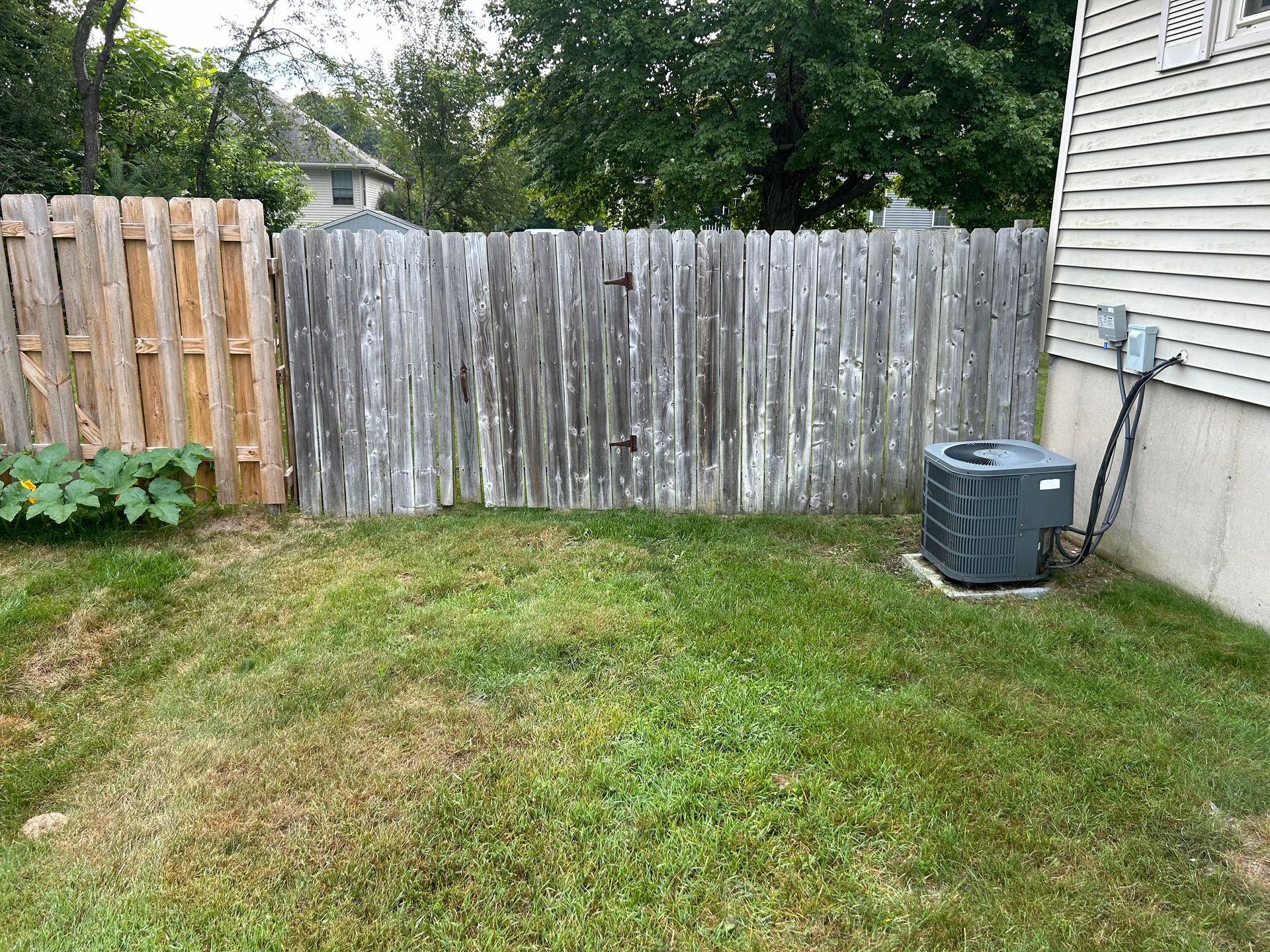 A backyard with a wooden fence and an air conditioner.