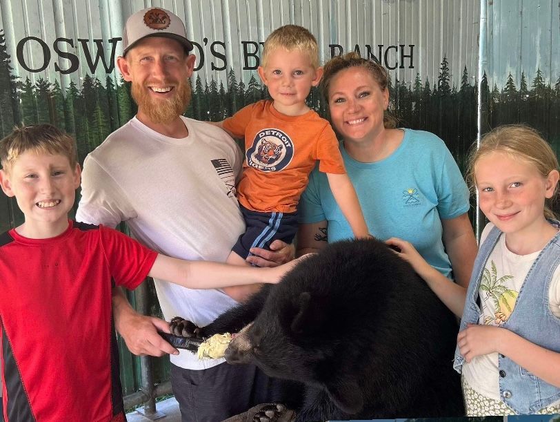 A family is posing for a picture with a stuffed bear.
