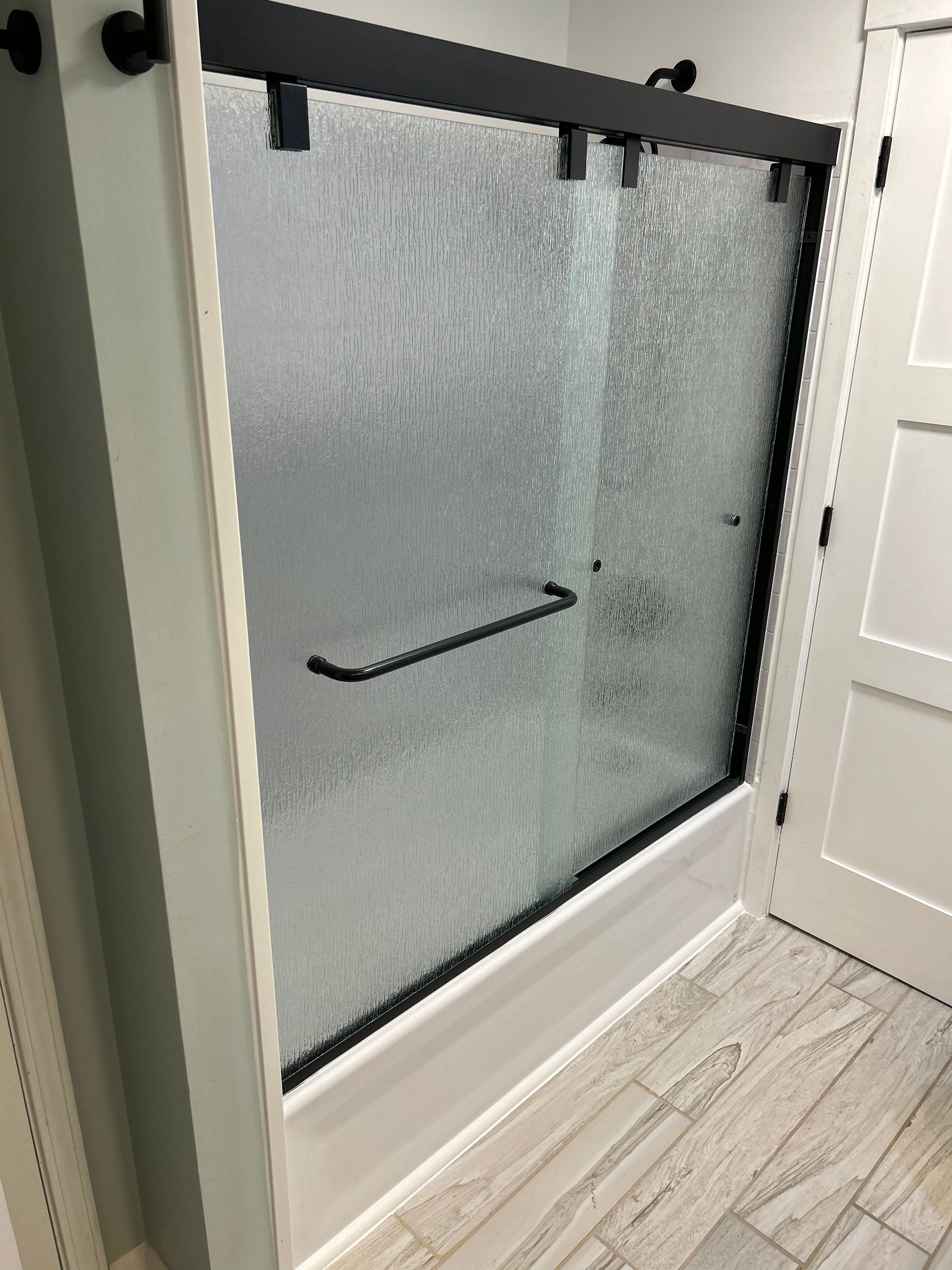 A bathroom with a sliding glass shower door and a black railing.