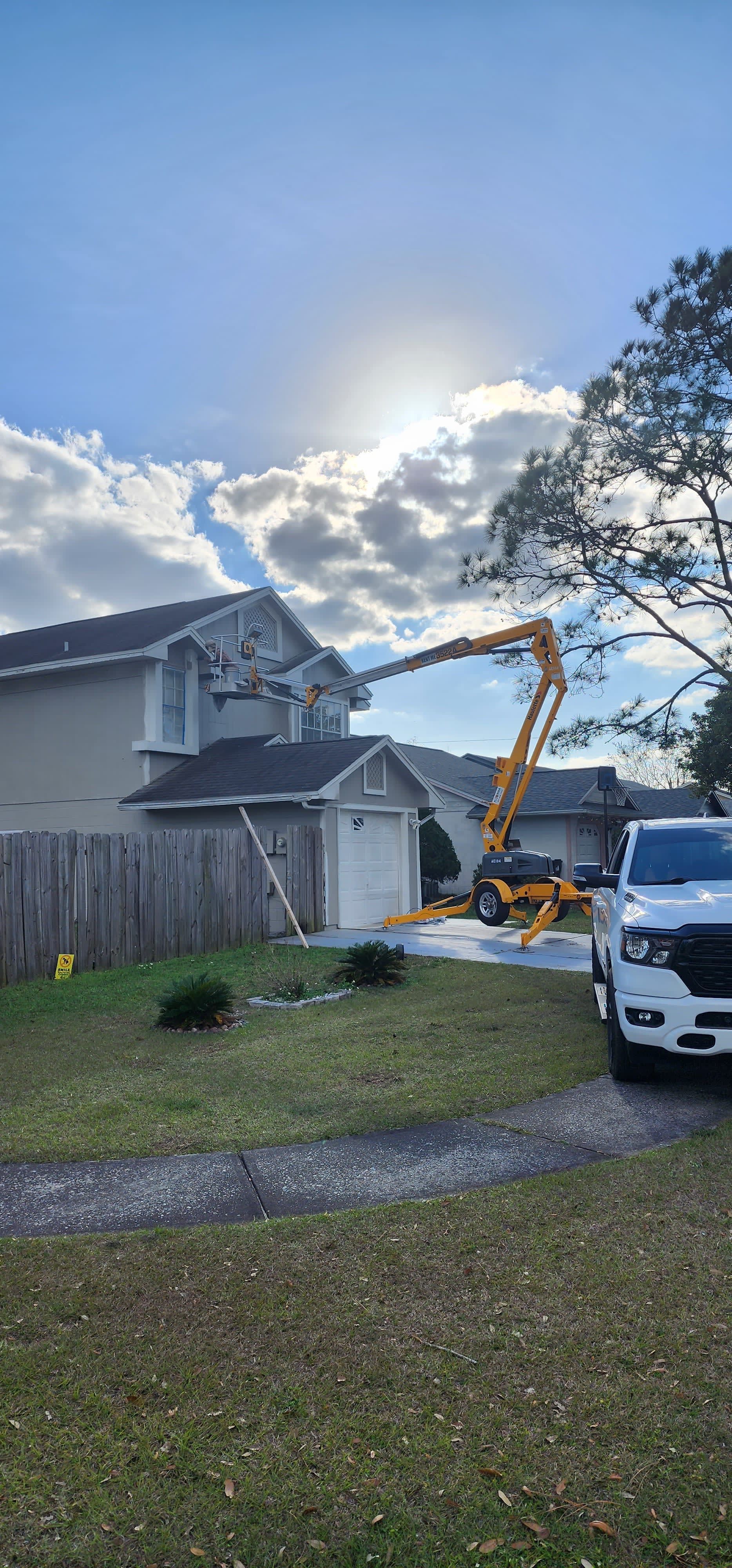 A white truck is parked in front of a house with a crane on the roof.