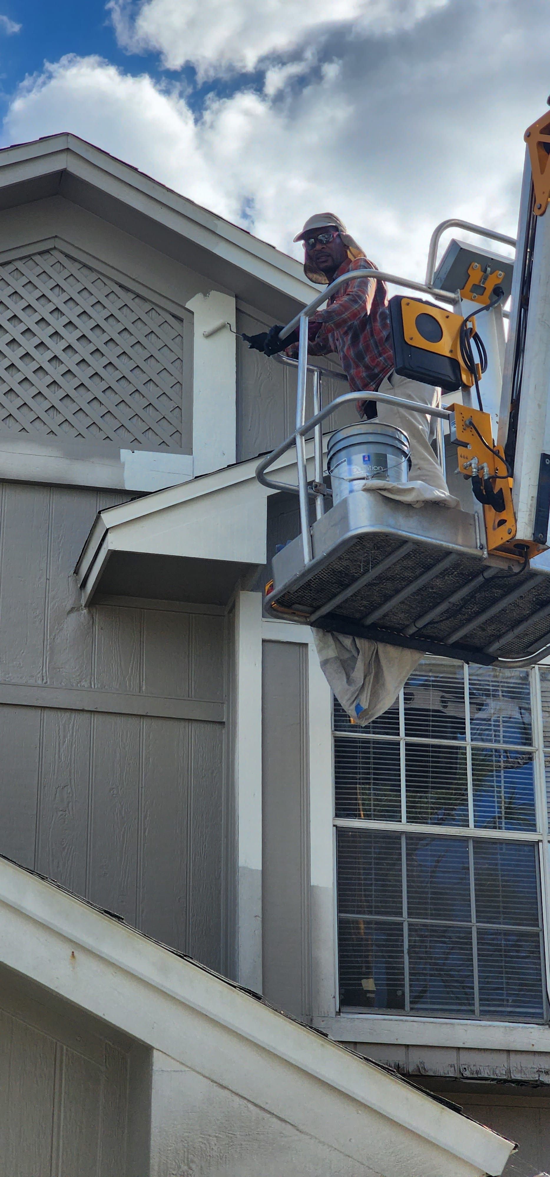 A man is painting the side of a house on a lift.