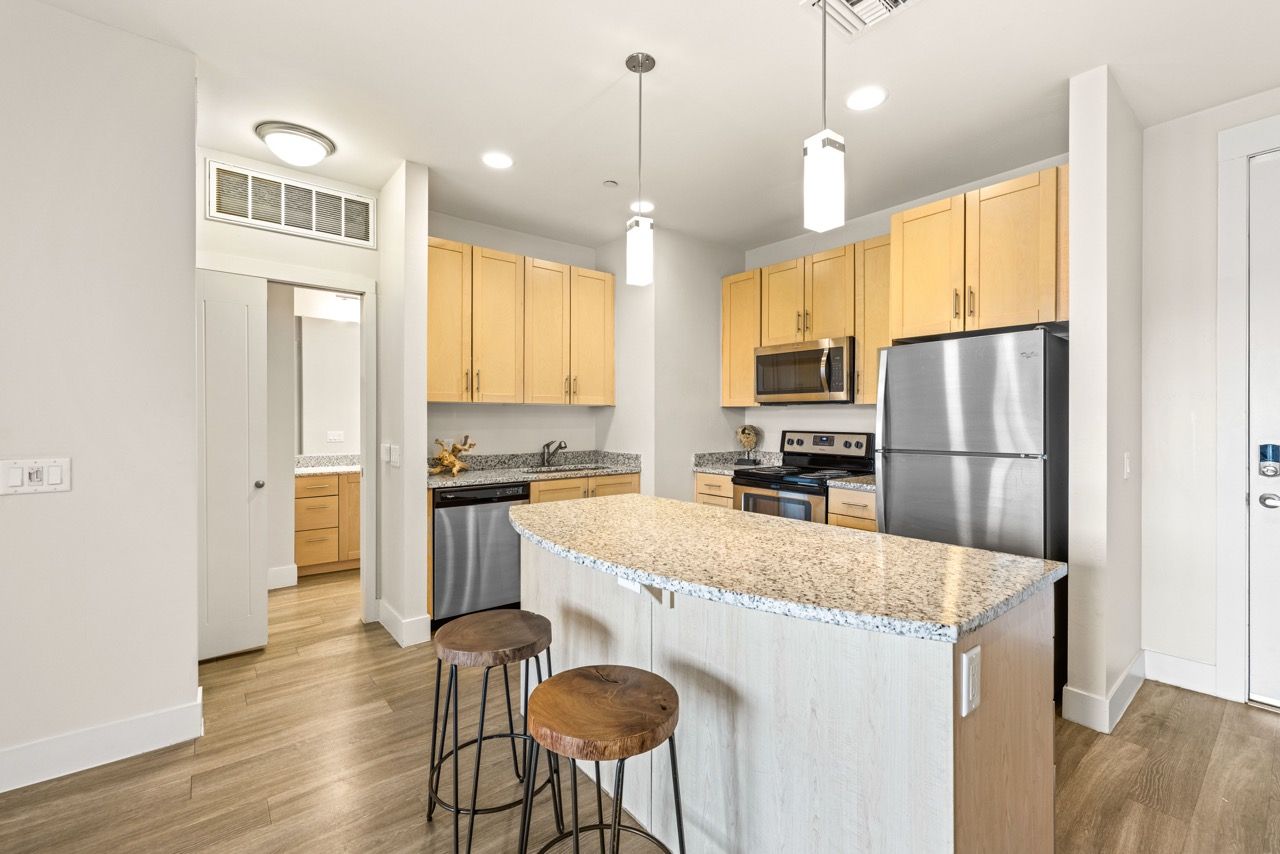 Open-concept kitchen with granite island, light wood cabinets, and stainless steel appliances at Mountain Trail, offering apartments in Flagstaff, AZ.