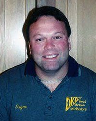 Smiling man in a dark polo shirt standing against a wood-paneled wall