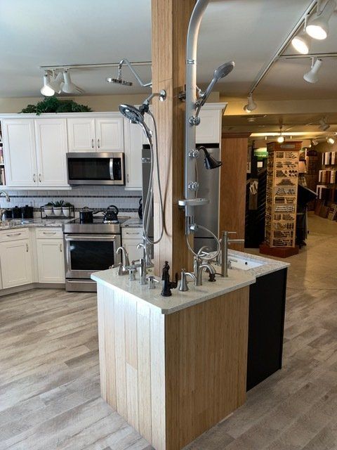 Modern kitchen showroom with white cabinets, stainless appliances, and a central wood island with sinks.