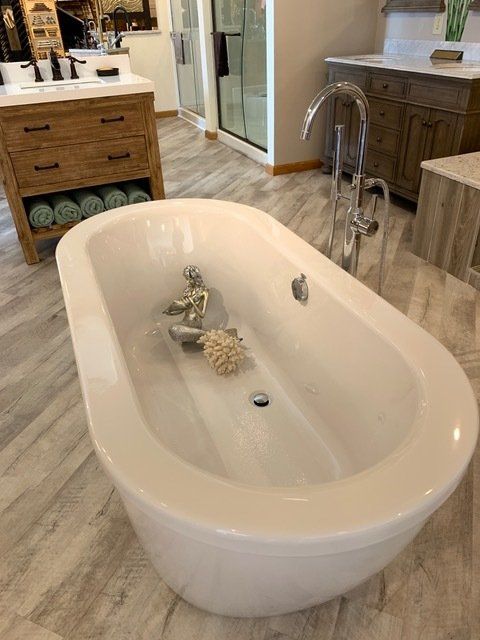 Freestanding white bathtub in a modern bathroom with wooden vanity and glass shower doors.