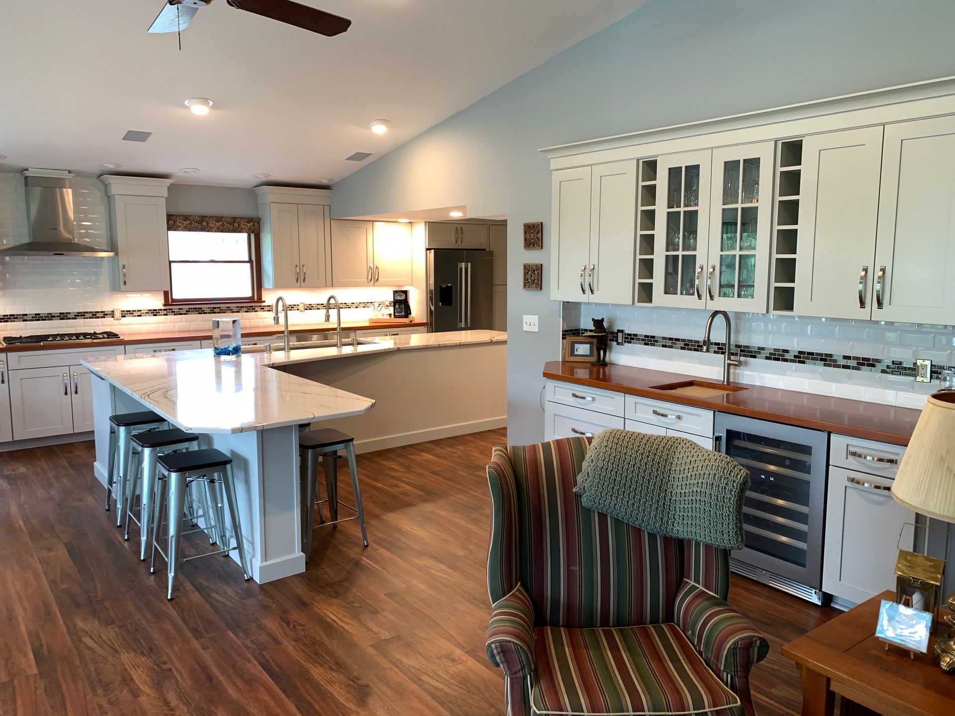 Bright modern kitchen with white cabinets, island seating, and wood floors; cozy chair in foreground