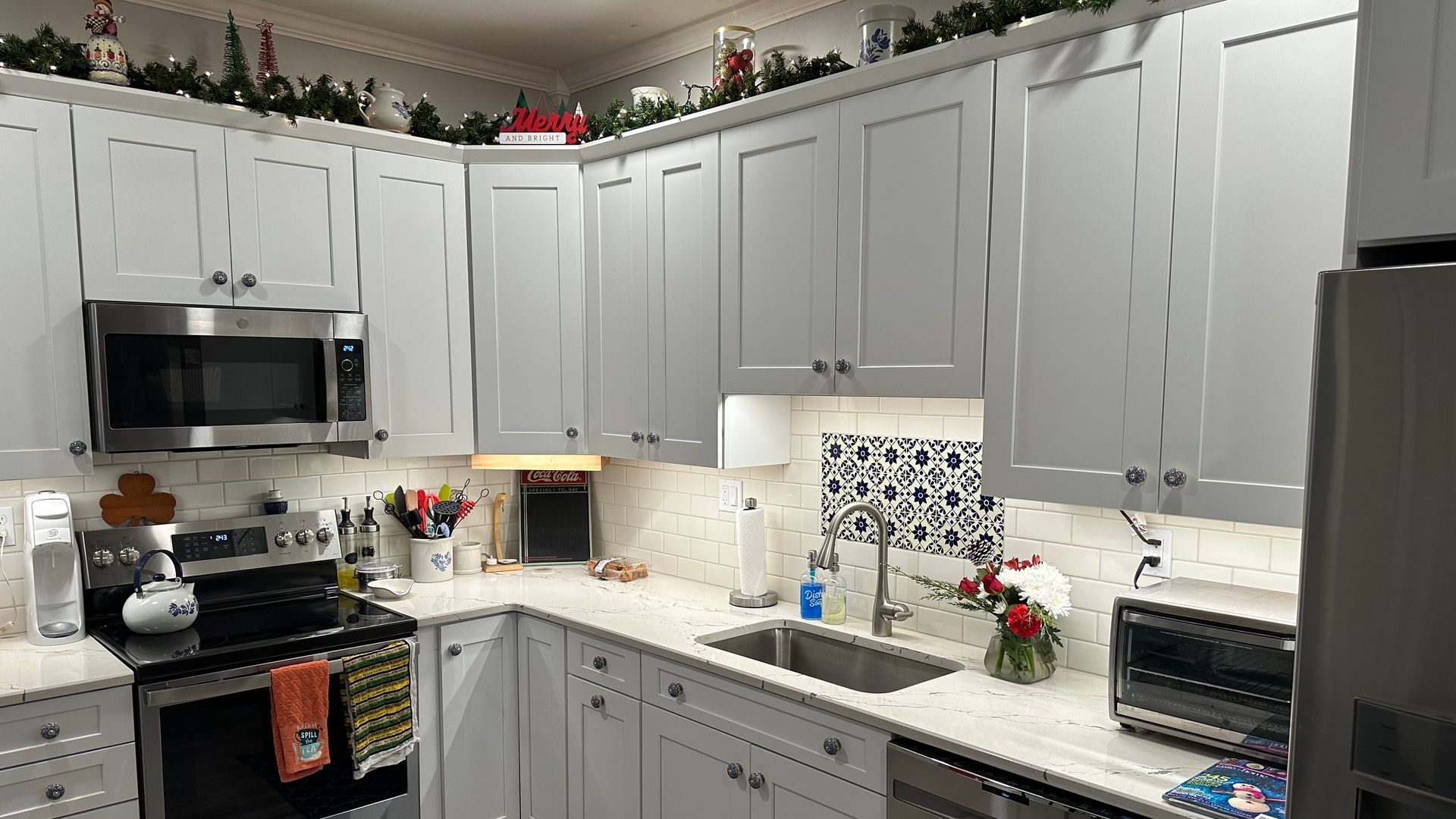 Bright kitchen with white cabinets, black stove, and speckled white countertops, decorated with flowers and greenery.