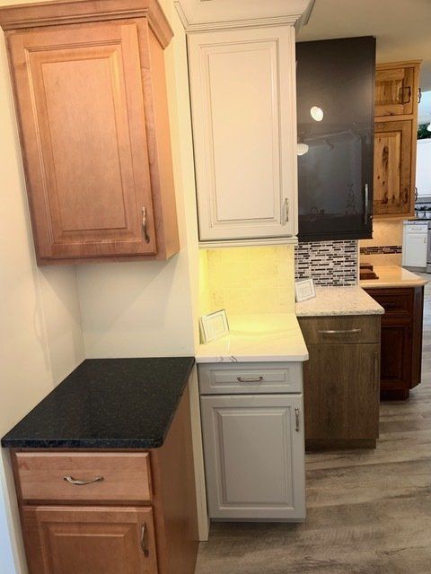 Kitchen cabinetry with black countertops, beige cabinets, and a tiled backsplash in a narrow corner.