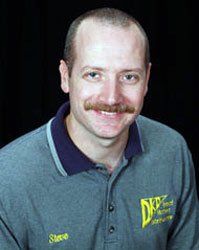 Portrait of a smiling man with a mustache in a gray collared shirt against a black background