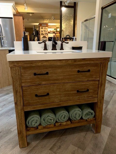 Wooden bathroom vanity with white countertop, black faucets, and rolled towels on the lower shelf.