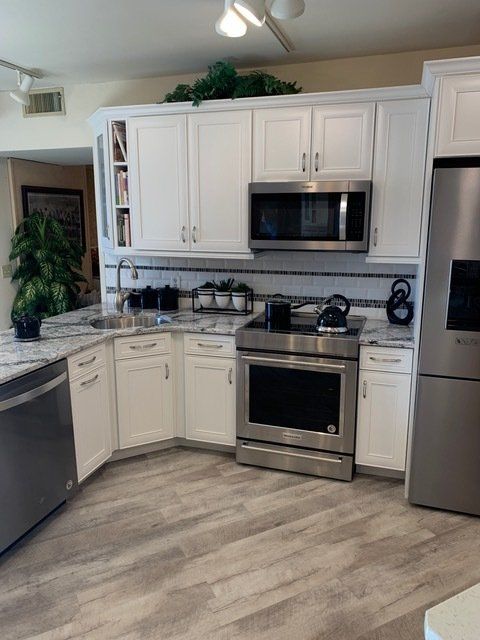 Modern kitchen with white cabinets, stainless steel appliances, granite counters, and light wood flooring