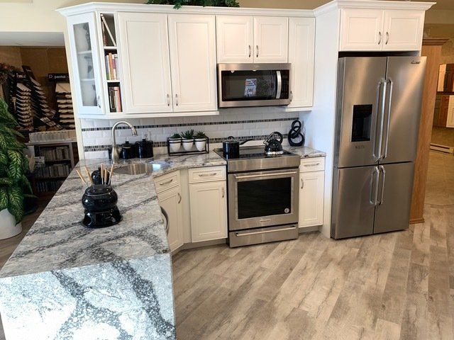 Modern kitchen with white cabinets, stainless appliances, granite countertops, and wood-look flooring