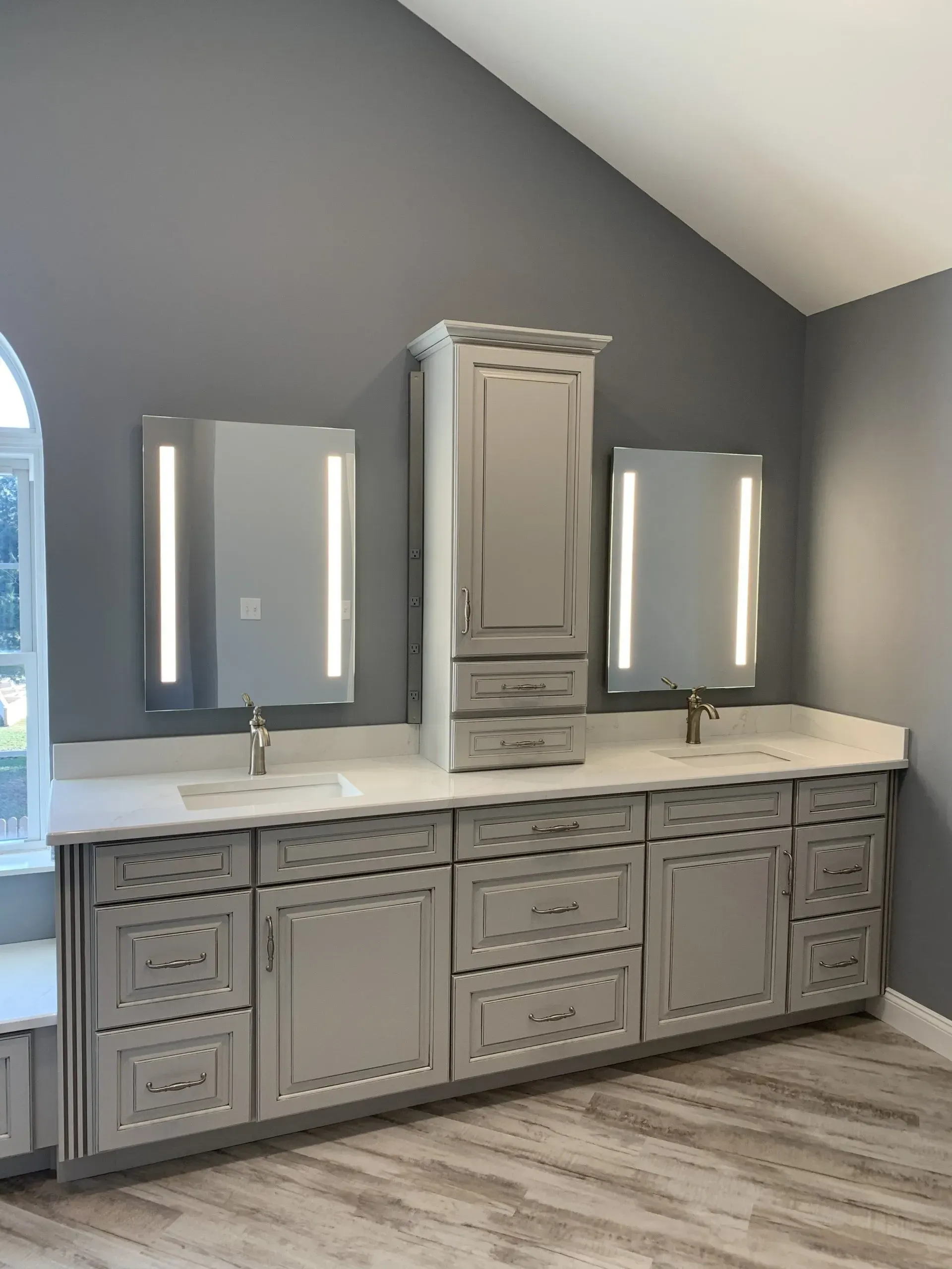 Modern double vanity bathroom with gray cabinets, white countertops, and wall mirrors beneath a sloped ceiling.
