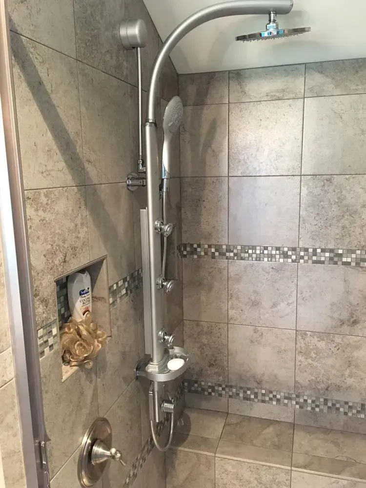 Accessible shower with grab bars, handheld showerhead, and tiled walls.
