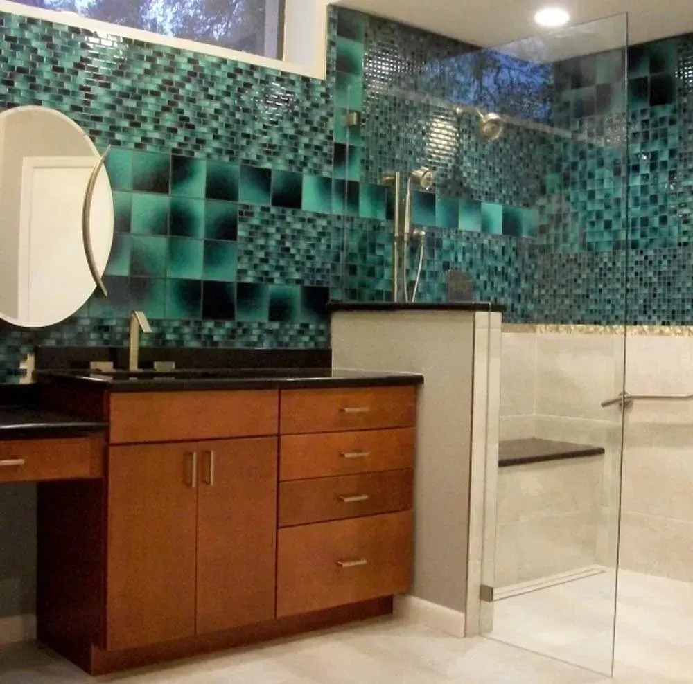 Modern bathroom with teal mosaic tile walls, wooden vanity, mirror, and glass shower enclosure