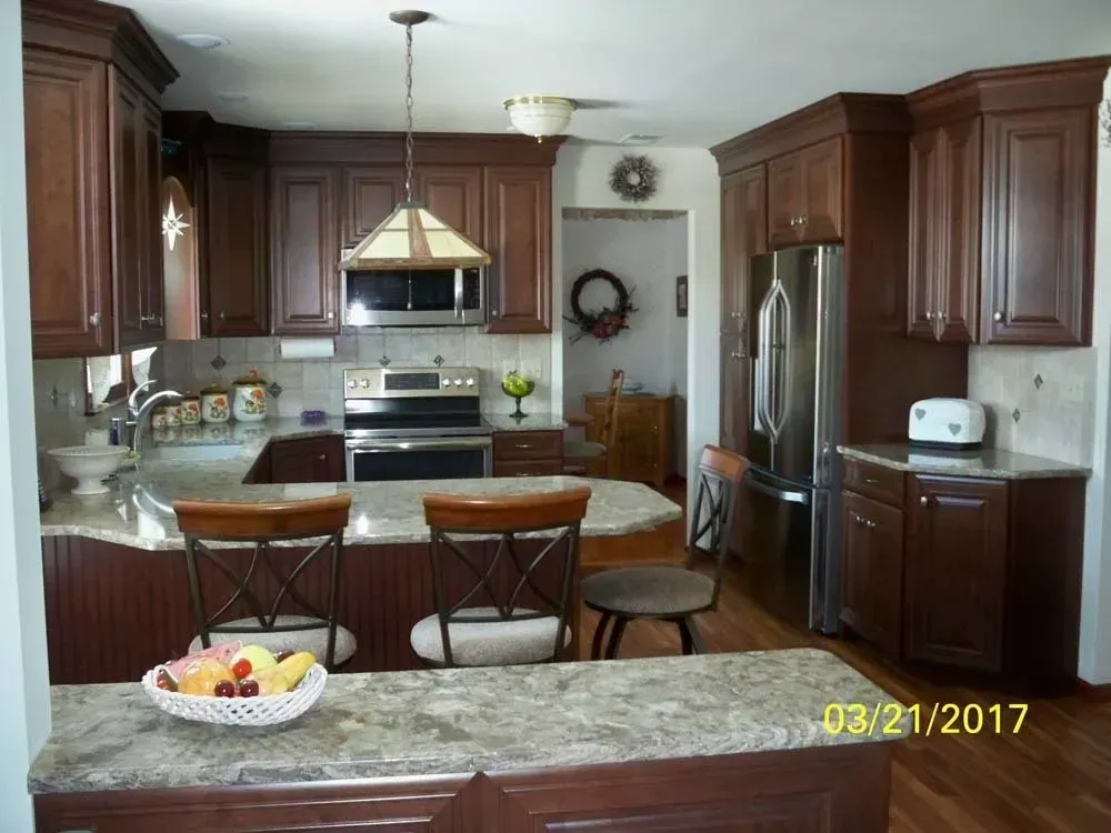 Kitchen with dark wood cabinets, stainless steel appliances, granite island, and a bowl of fruit on the counter.