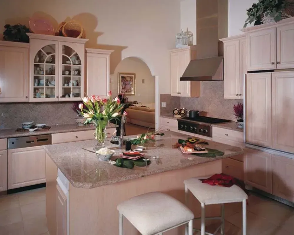 Bright cream kitchen with island, flowers, white cabinets, and stainless range under a hood