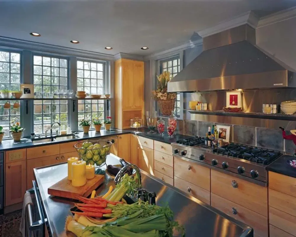 Bright kitchen with large windows, wood cabinets, stainless range, and vegetables on a central island.