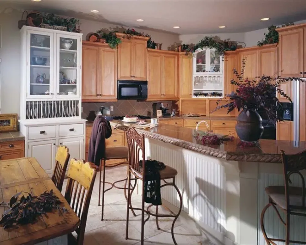 Bright kitchen with light wood cabinets, white island, bar stools, and flowers on a granite countertop.