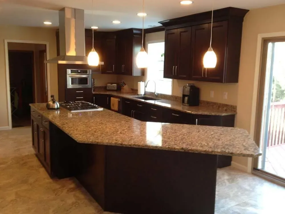 Modern kitchen with dark cabinets, granite island, pendant lights, and stainless steel appliances.