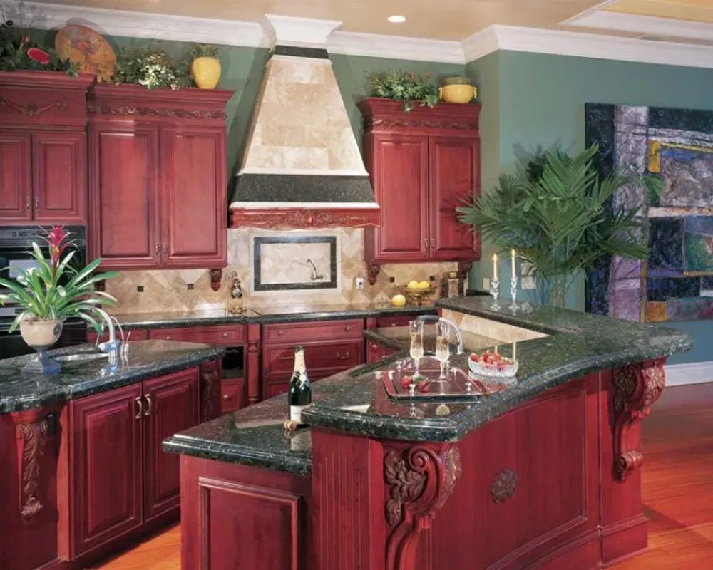 Elegant kitchen with red wood cabinets, green granite counters, island, and decorative hood surround