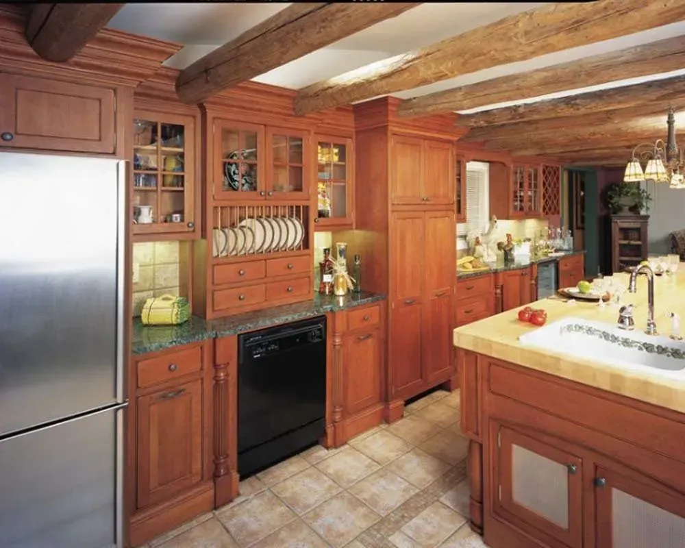 Warm wood kitchen with stainless steel refrigerator, black dishwasher, and tiled island under ceiling beams.