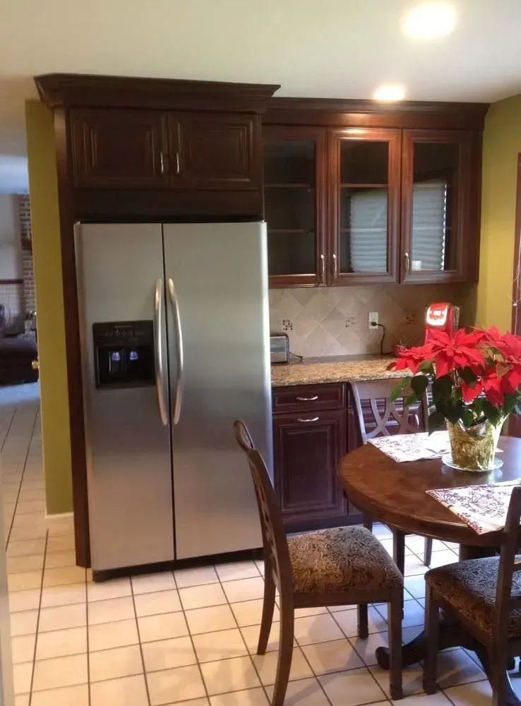 Kitchen with stainless steel fridge, dark wood cabinets, tile floor, and a round table with red flowers.