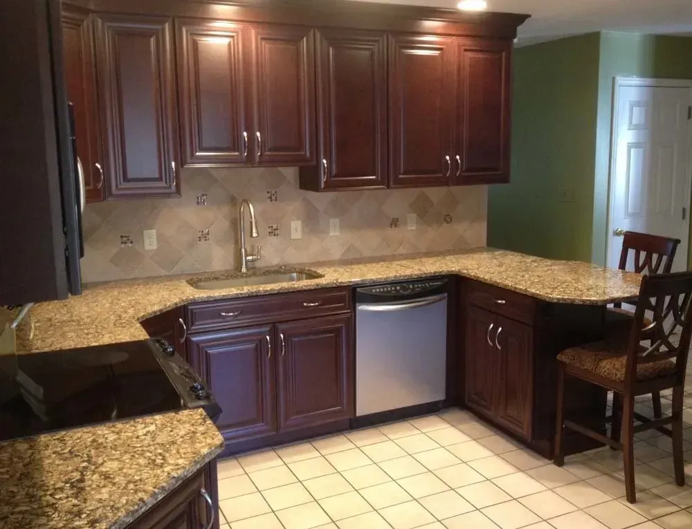 Kitchen with dark wood cabinets, tan countertops, tile floor, and a stool by a green wall.