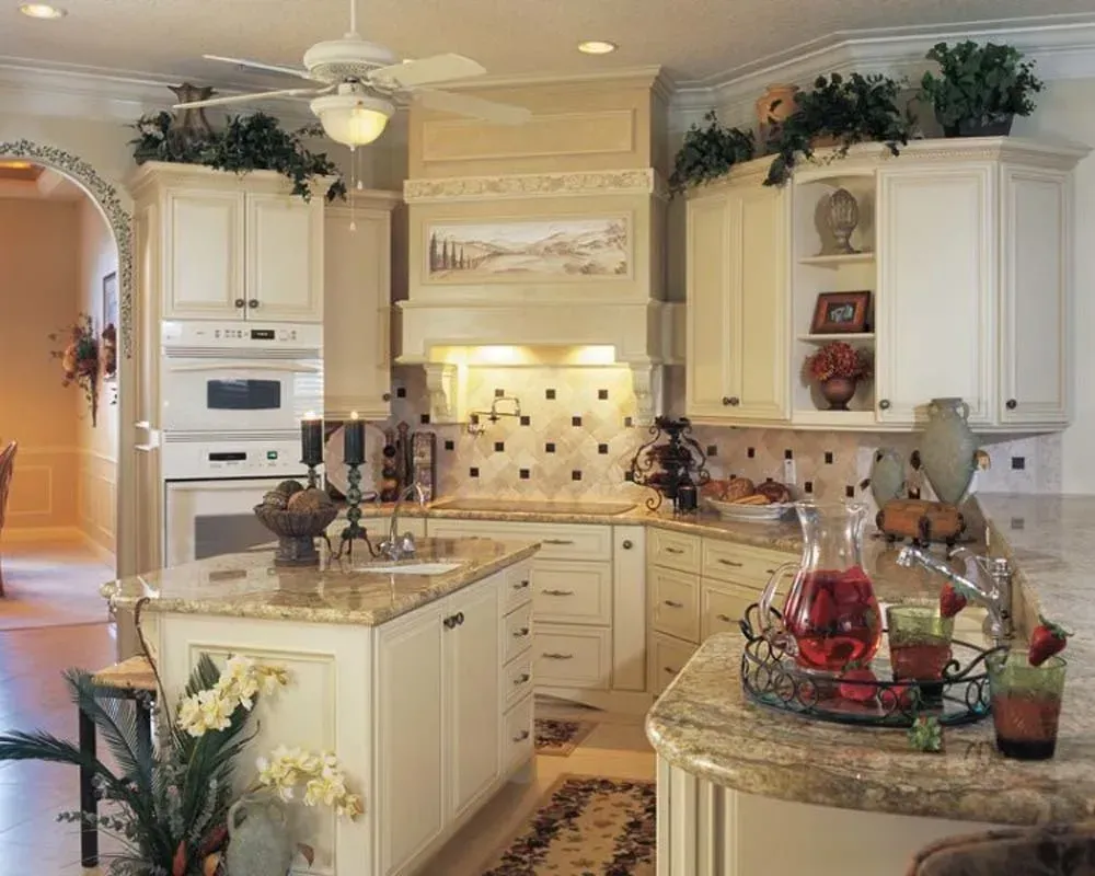 Elegant cream-colored kitchen with marble island, white cabinets, and decorative plants and red accents