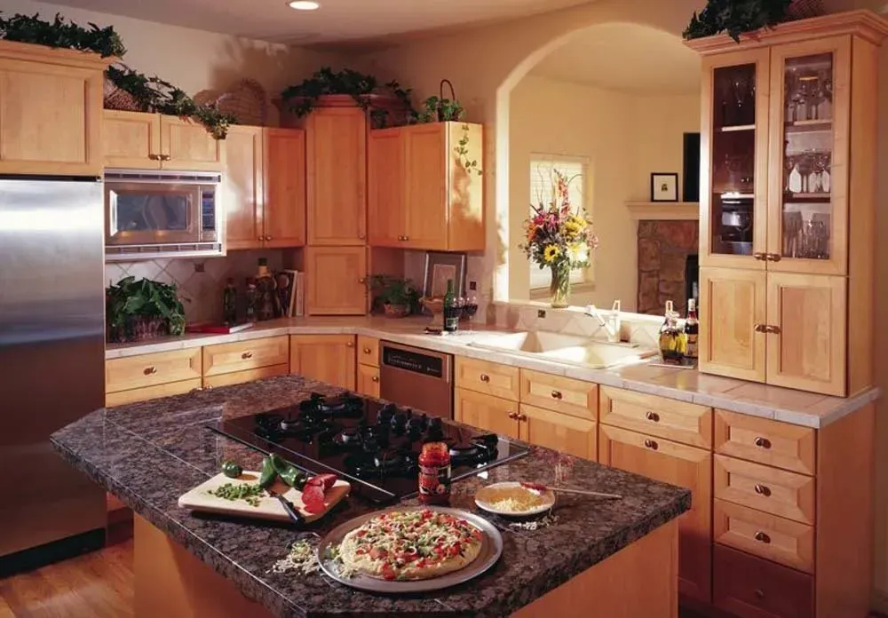 Warm kitchen with wood cabinets, granite island, and a set dining table near a bright arched window.