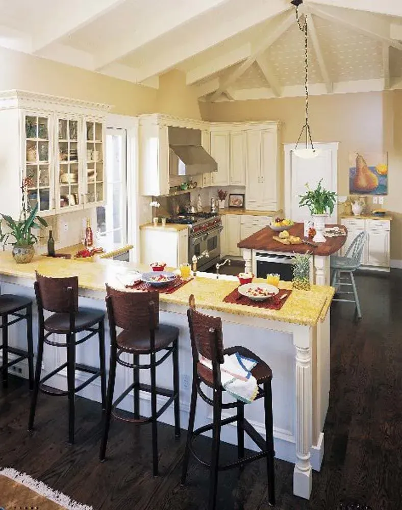 Bright kitchen with island breakfast bar, dark stools, white cabinets, and red table settings