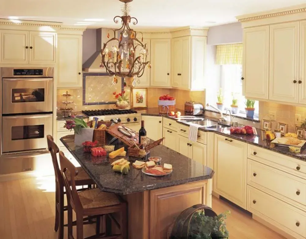 Bright, modern kitchen with cream cabinets, granite island, chandelier, and a table set with food.