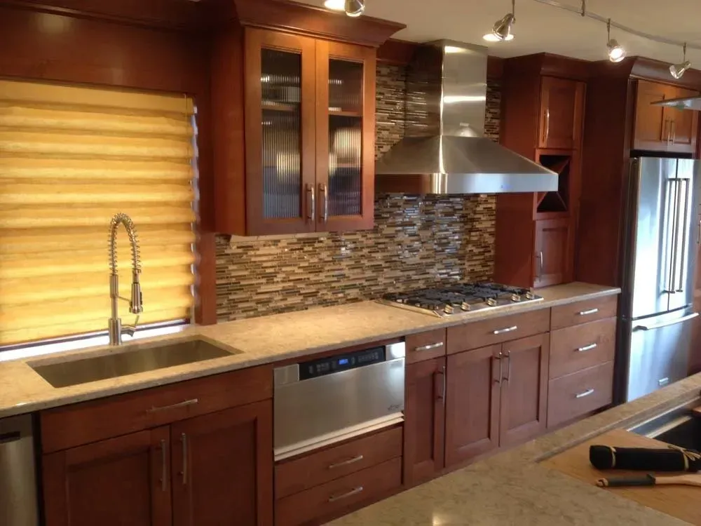Modern kitchen with dark wood cabinets, stone backsplash, stainless range hood, sink, and window blinds