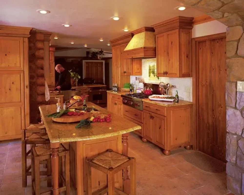 Warm rustic kitchen with wooden cabinets, stone walls, central island, and a person preparing food