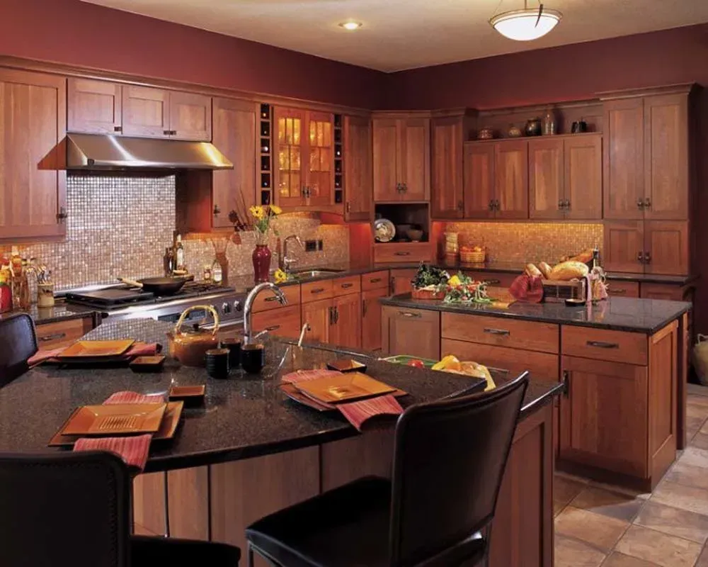 Warm wood kitchen with island, stainless range hood, black chairs, and fruit on counters