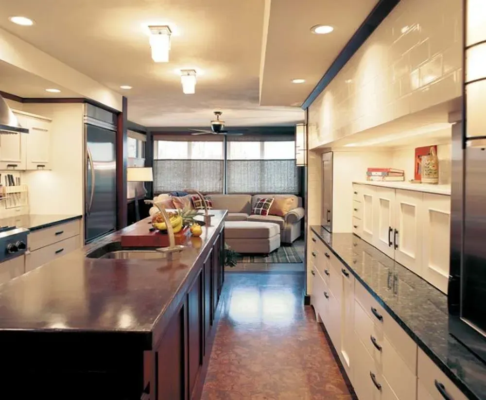 Modern galley kitchen with dark island, white cabinets, and a breakfast nook beyond