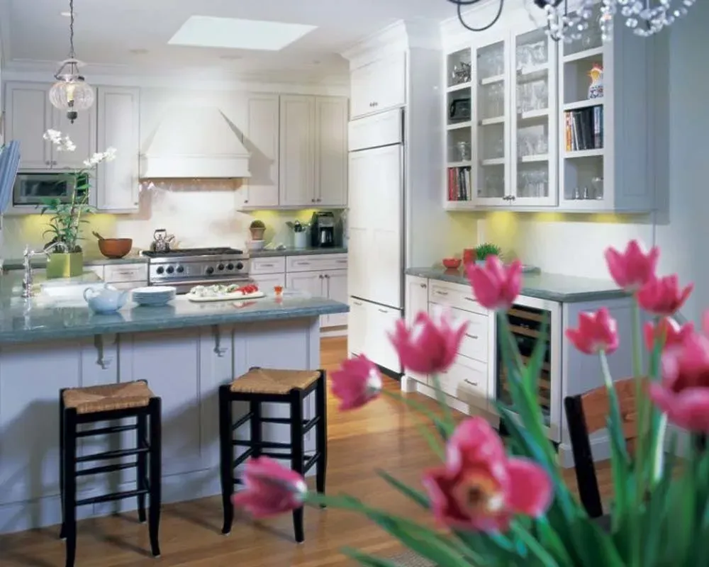 Bright modern kitchen with white cabinets, blue island, stools, and pink flowers in the foreground