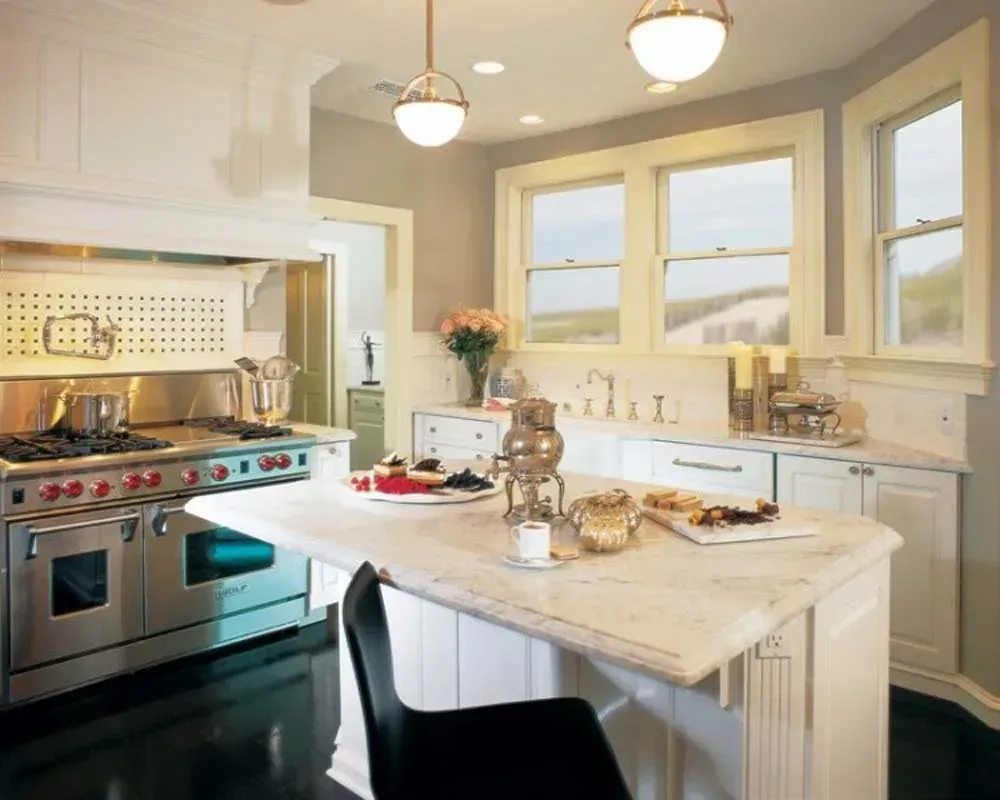 Bright modern kitchen with stainless steel stove, marble island, and large windows overlooking mountains